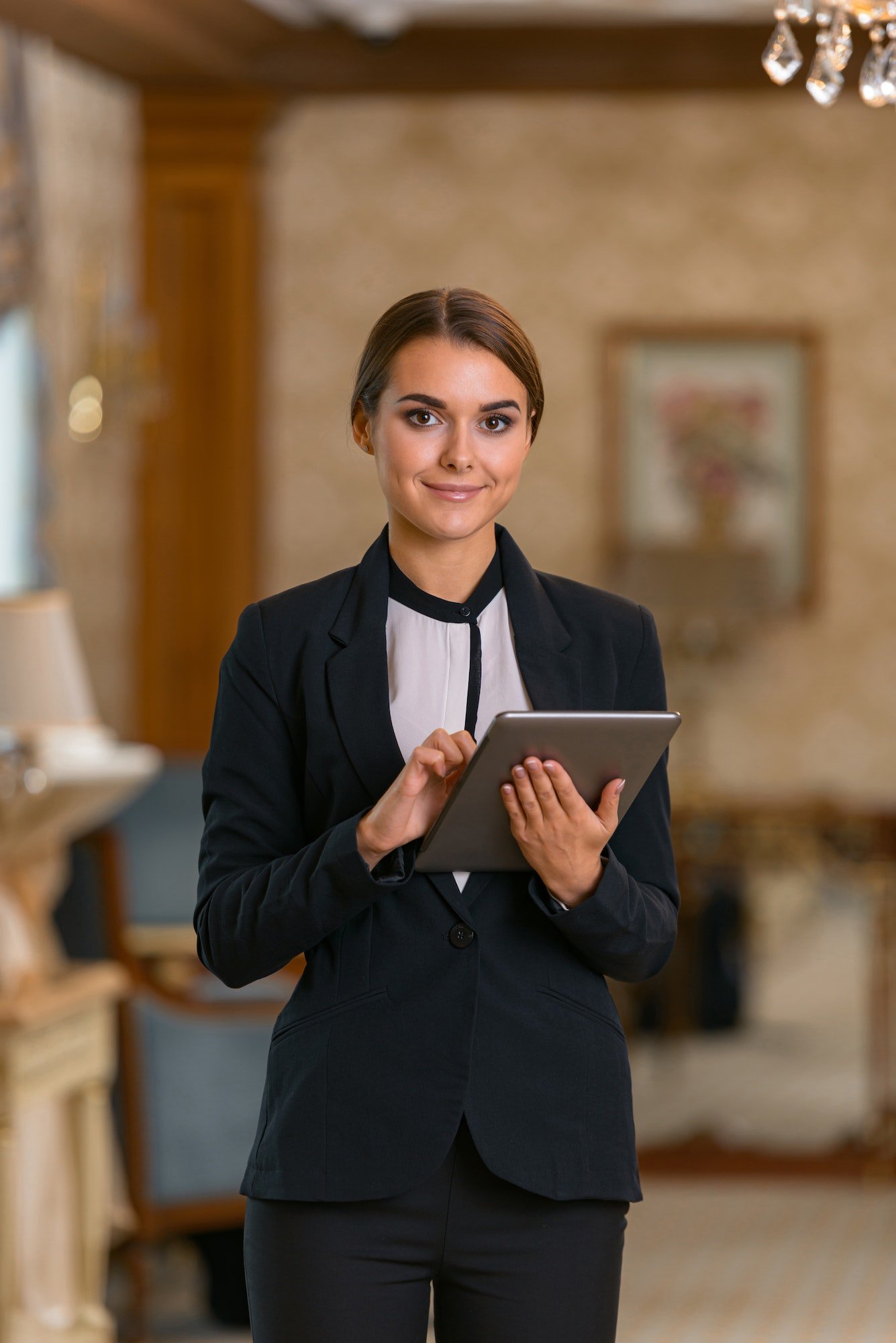 smiling-businesswoman-in-suit-standing-in-hotel-room-using-digital-tablet-and-looking-camera.jpg